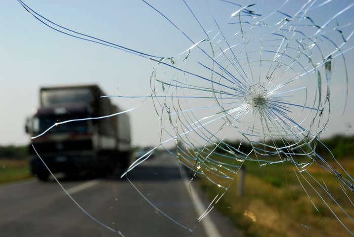 Cracked windshield with focus on impact point, a truck is visible on the road in the background