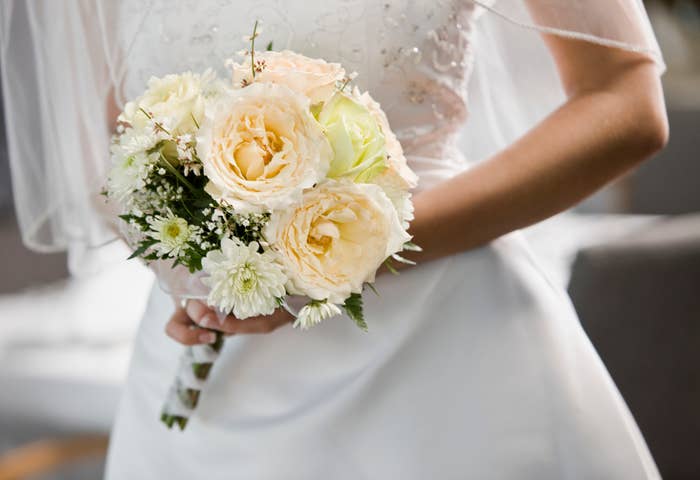 A bride holds a bouquet of flowers, wearing a wedding dress with intricate detailing