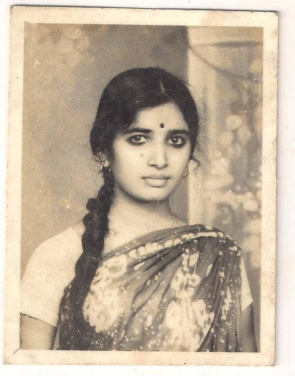 A black-and-white portrait of a woman with a long braid, wearing a traditional sari with floral patterns and earrings