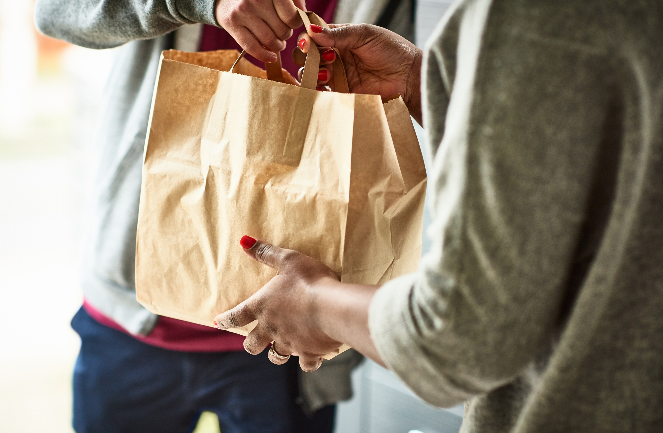 Two people exchange a paper bag, focusing on their hands