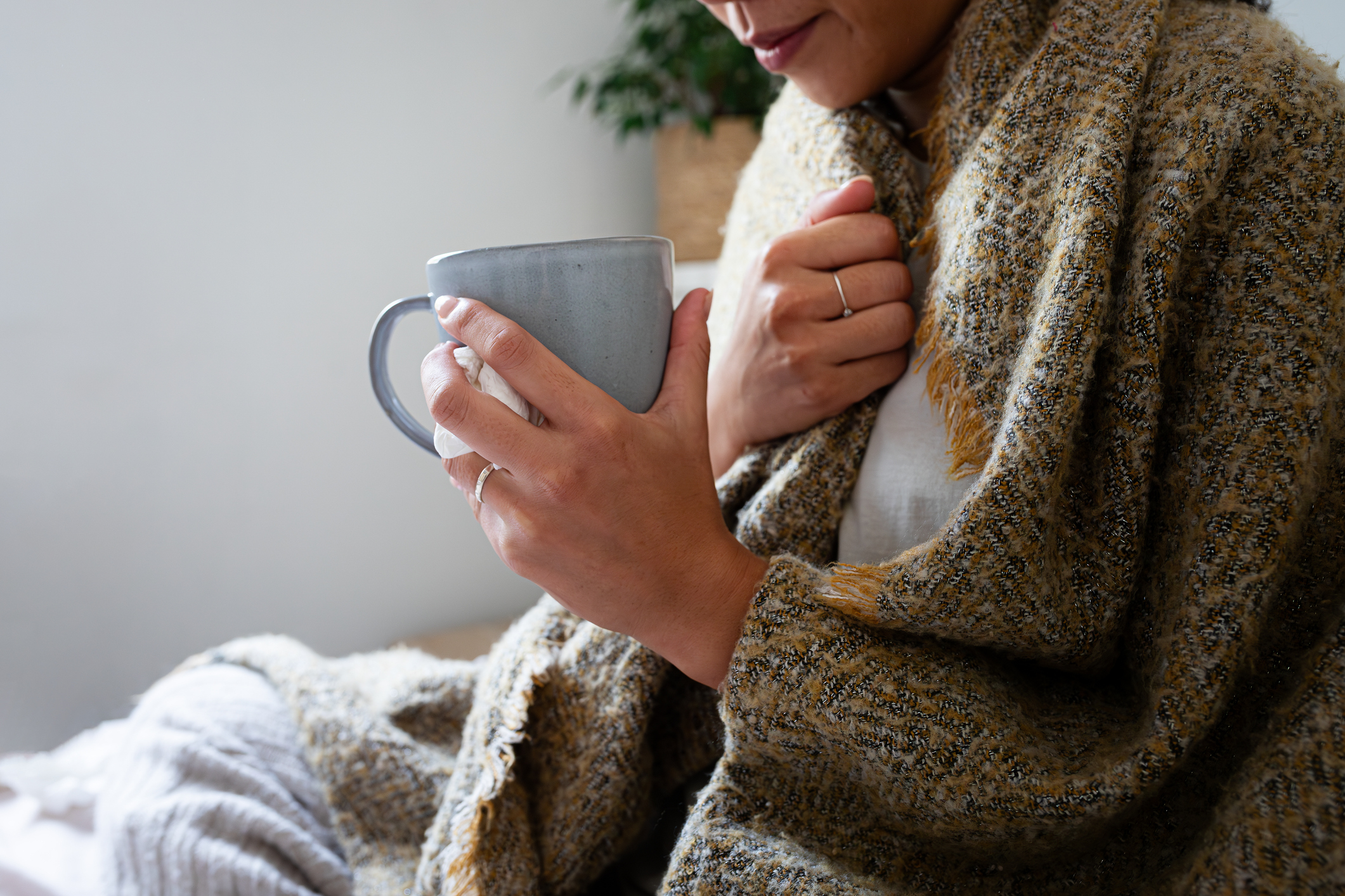 A person sits wrapped in a blanket, holding a mug close to their chest, with a relaxed expression on their face