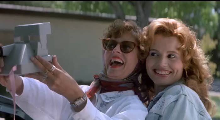 Susan Sarandon and Geena Davis in a scene from "Thelma & Louise", taking a selfie with a Polaroid camera and smiling