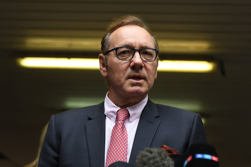 I don't know who this is. A man in a suit and tie stands in front of some microphones, giving a speech or interview