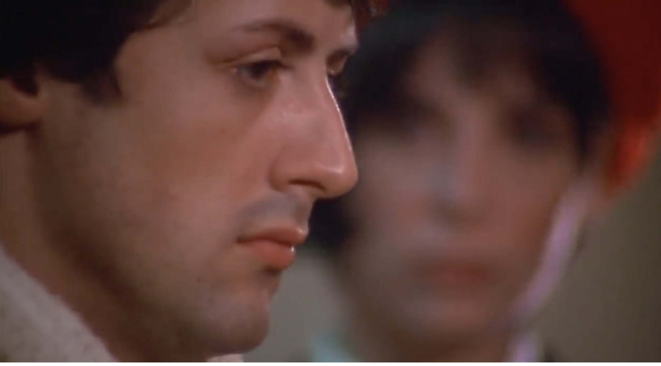 A close-up of Sylvester Stallone, with another person blurred in the background