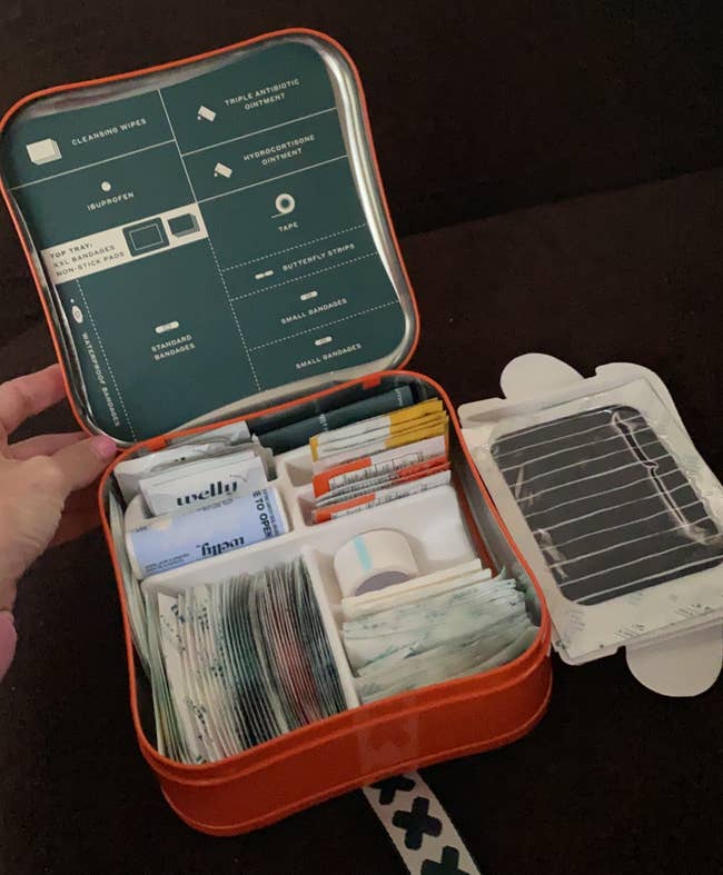 First assistance kit with unfastened lid showing organized aesculapian supplies including bandages, antiseptic wipes, and assorted medications
