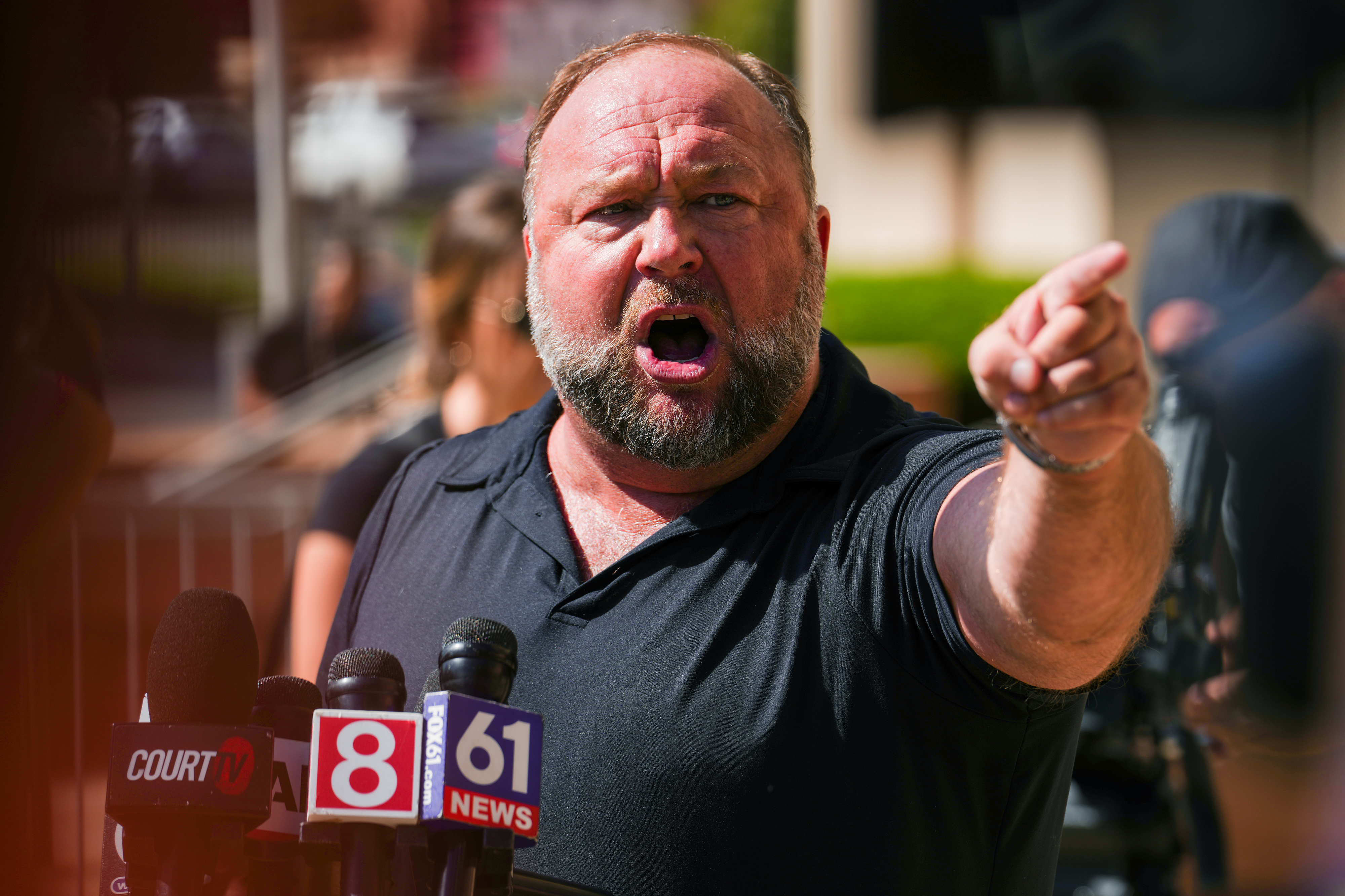 Man passionately speaking and pointing during a press conference with several microphones in front