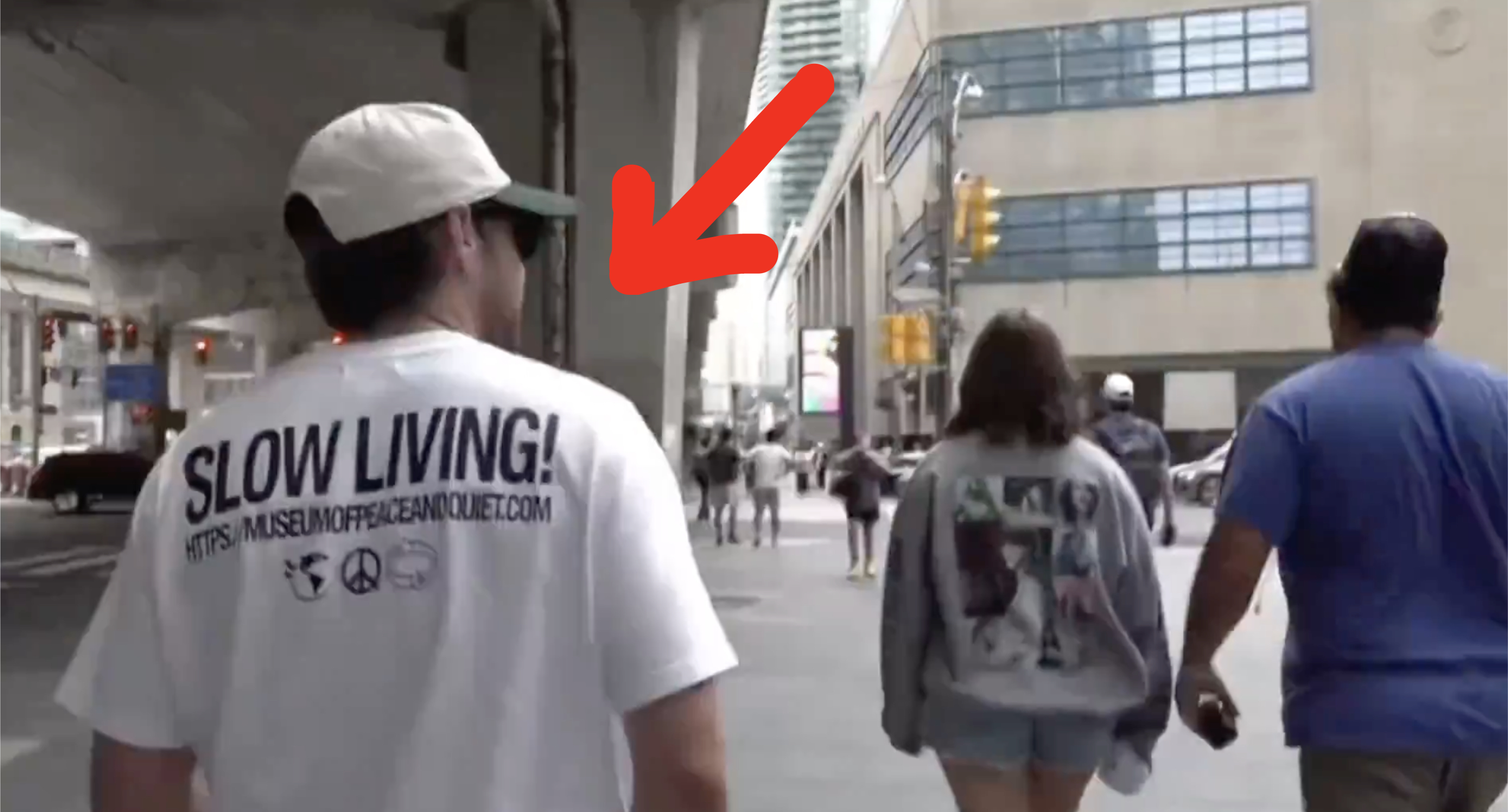 A man walks under an overpass in a shirt that says "SLOW LIVING!" followed by peace sign and recycling symbols