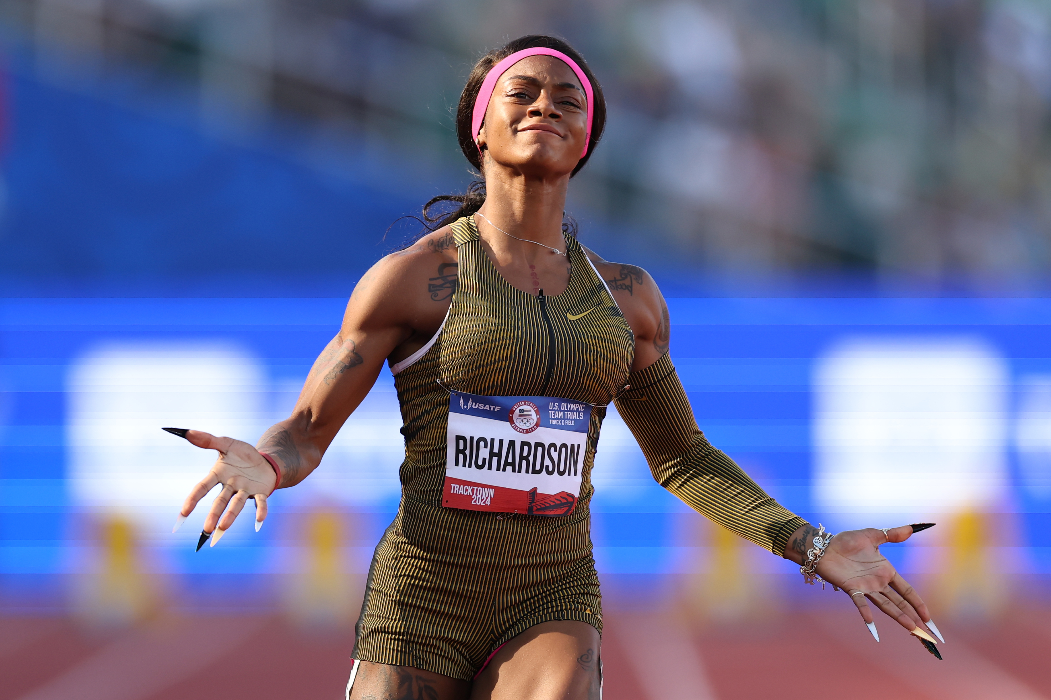 Sha&#x27;Carri Richardson gestures triumphantly on the track, wearing a striped athletic outfit and headband