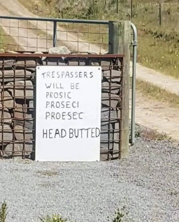 A handwritten sign on a gate reads, "Trespassers will be prosic proseci proesec head butted." It appears to warn trespassers with humor