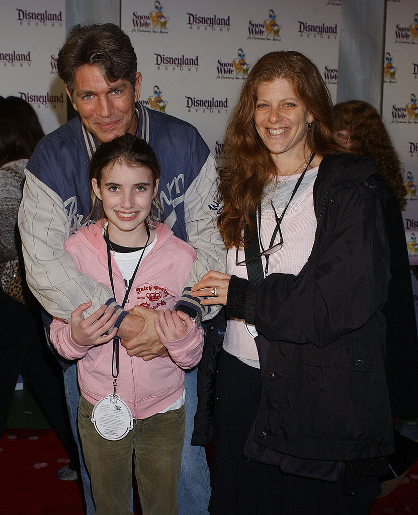 Eric Roberts, Emma Roberts, and Kelly Cunningham are on a red carpet. Eric wears a casual jacket, Emma a pink hoodie, and Kelly a casual jacket. All are smiling