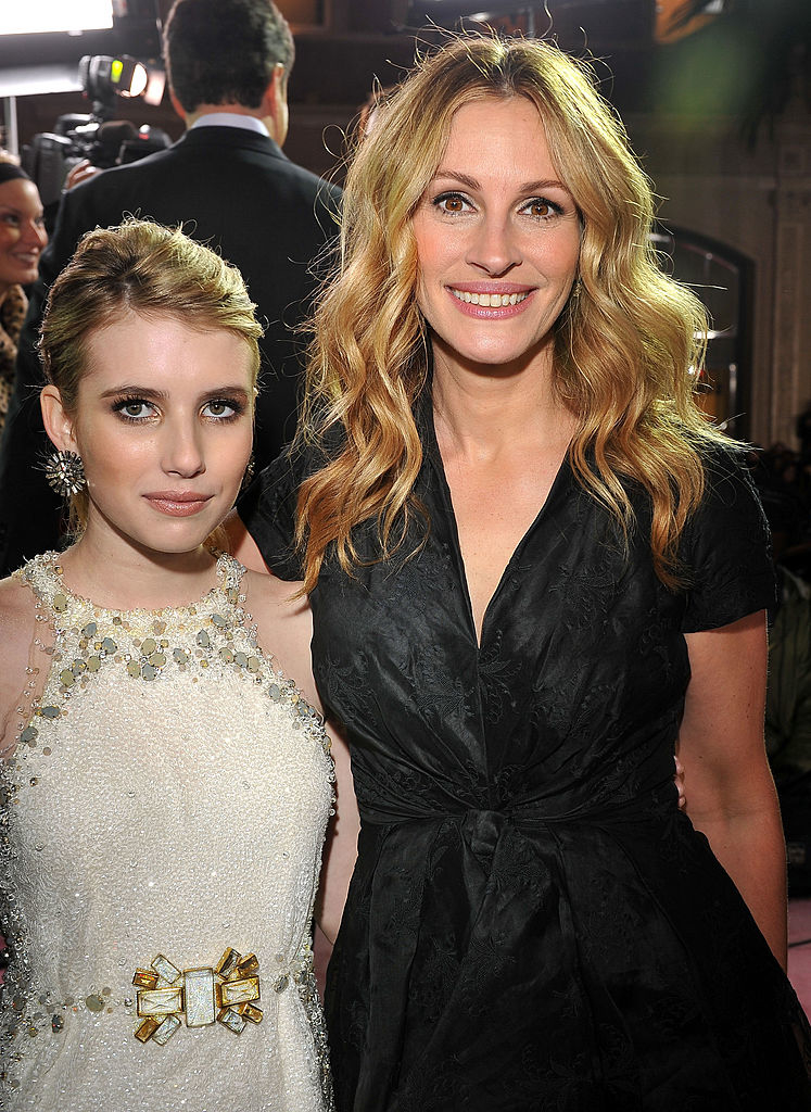 Julia Roberts in a black dress and Emma Roberts in a white gown smiling at a public event