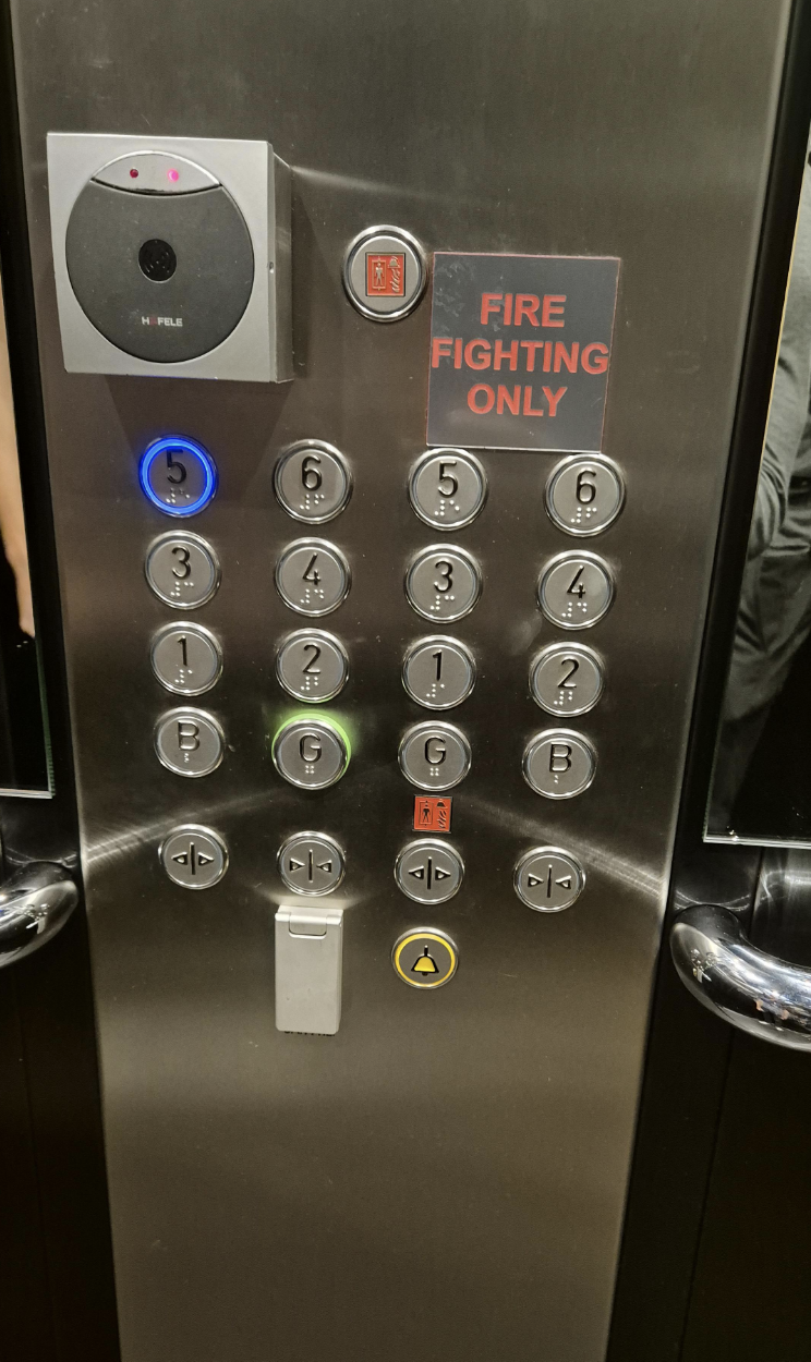 Elevator control panel with 15 buttons, including a &quot;Fire Fighting Only&quot; sign, emergency call button, and floor numbers; buttons are arranged in a vertical grid