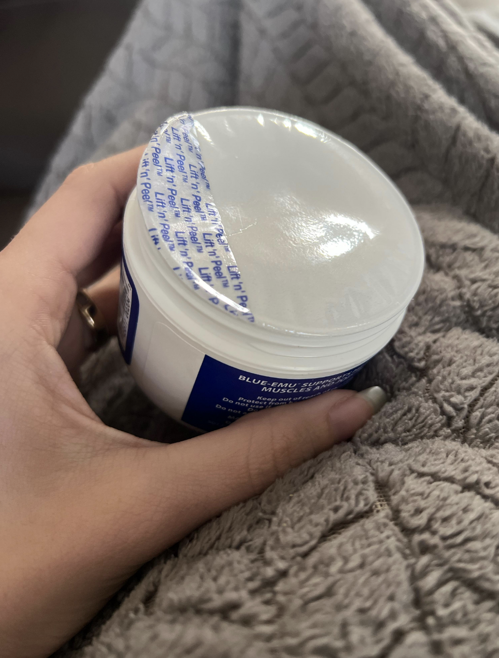 A hand holds an opened container of Blu Lizard Australian Sunscreen with a partially peeled foil seal