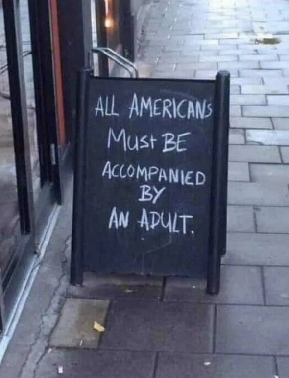 Sign on a sidewalk reads, "ALL AMERICANS MUST BE ACCOMPANIED BY AN ADULT."
