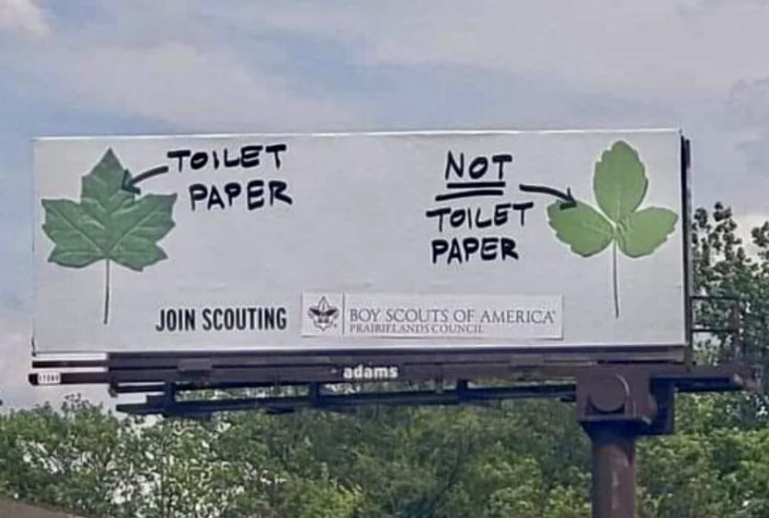 A billboard shows a comparison between two leaves: one labeled "Toilet Paper" and the other "Not Toilet Paper," promoting the Boy Scouts of America
