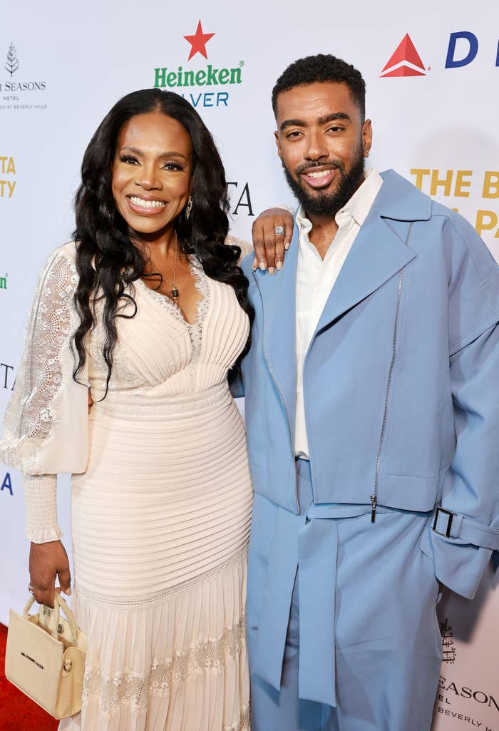 Sheryl Lee Ralph in a white dress and her son Etienne Maurice in a light blue suit smile together on the red carpet at an event