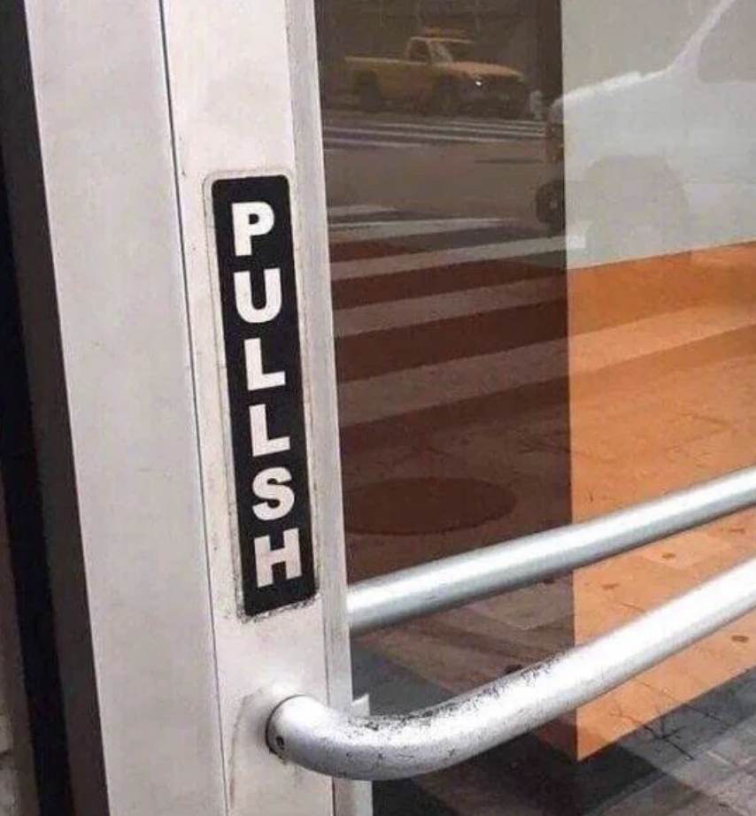 Sign on a glass door reads "PULLSH" instead of "PULL." A person is visible outside by the crosswalk. A humorous misspelling of the word "PULL."
