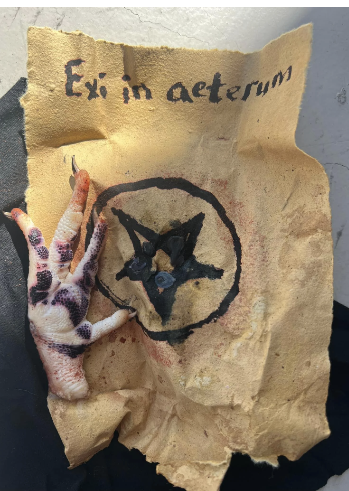 A parchment with "Ex in aeternum" written on it, featuring a pentagram and a severed, gory, clawed hand next to it