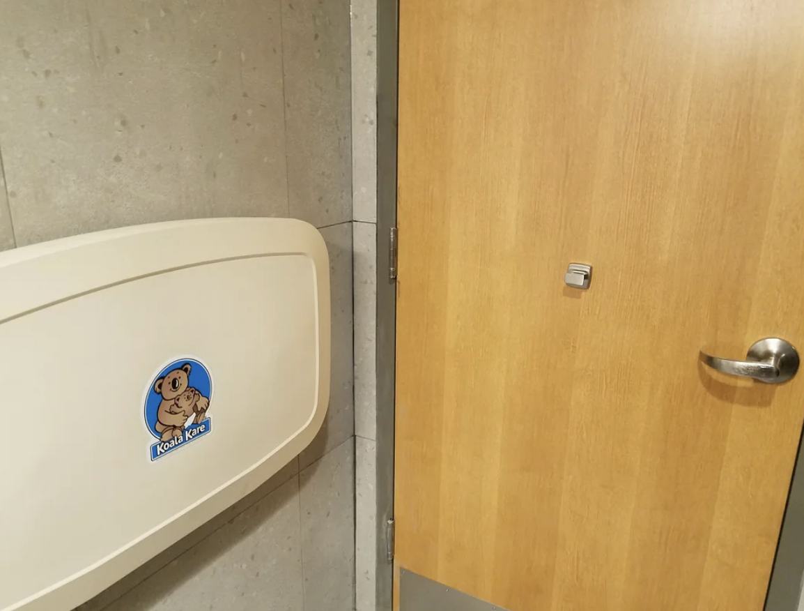 Image of a Koala Kare baby changing station next to a wooden door in a restroom