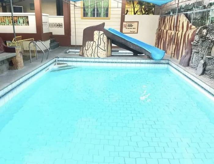 A nearly empty swimming pool with a blue slide beside it. There are buildings and murals in the background