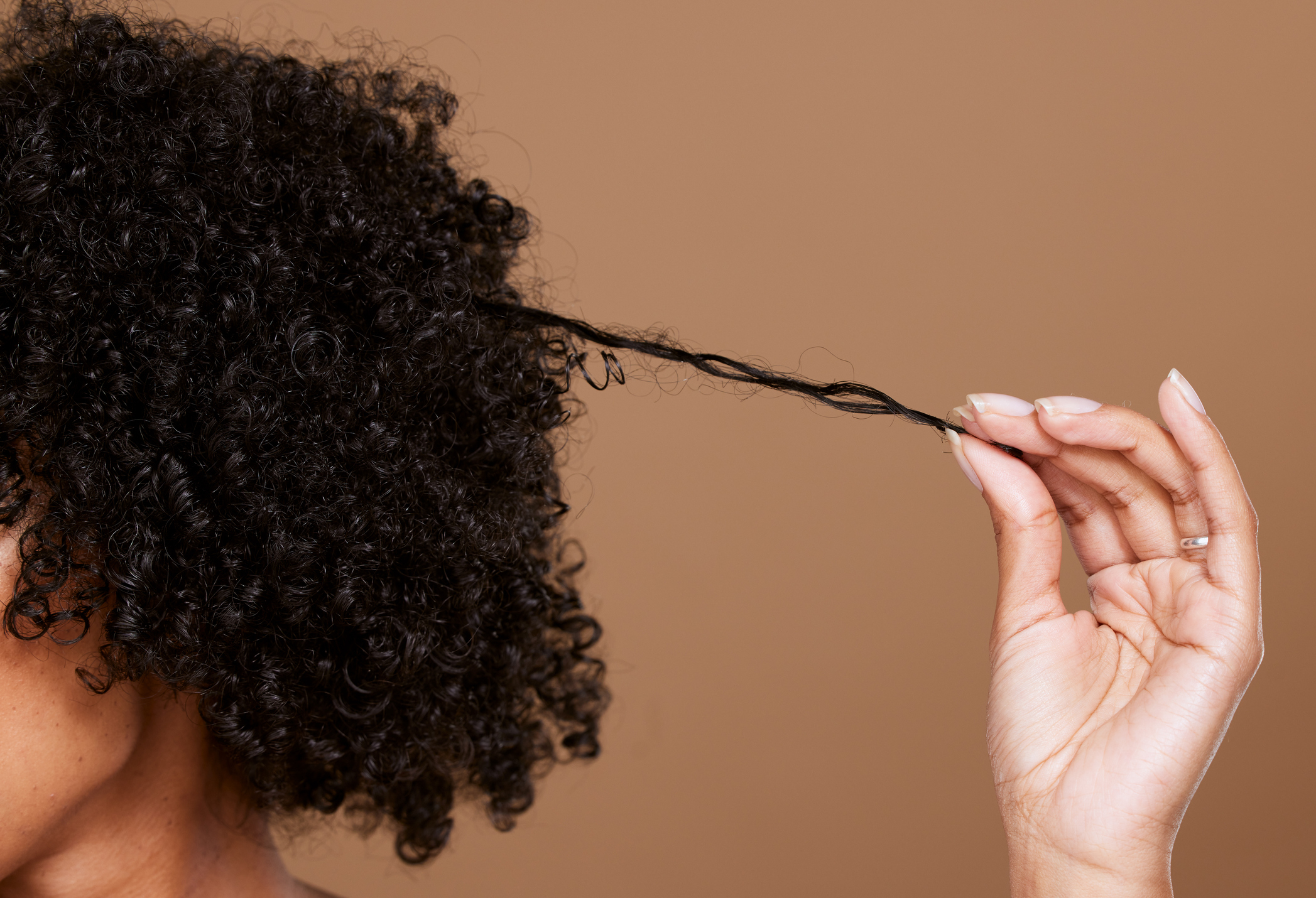 A person gently pulls a strand of their curly hair