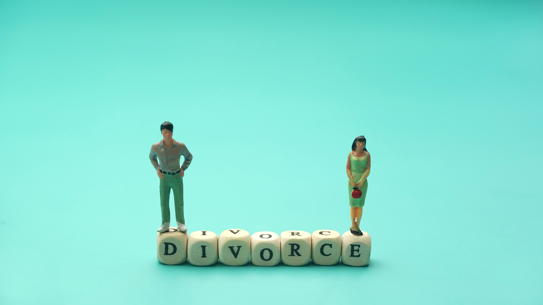 Two small figurines, a man and a woman, stand on alphabet blocks spelling "DIVORCE" against a gradient background