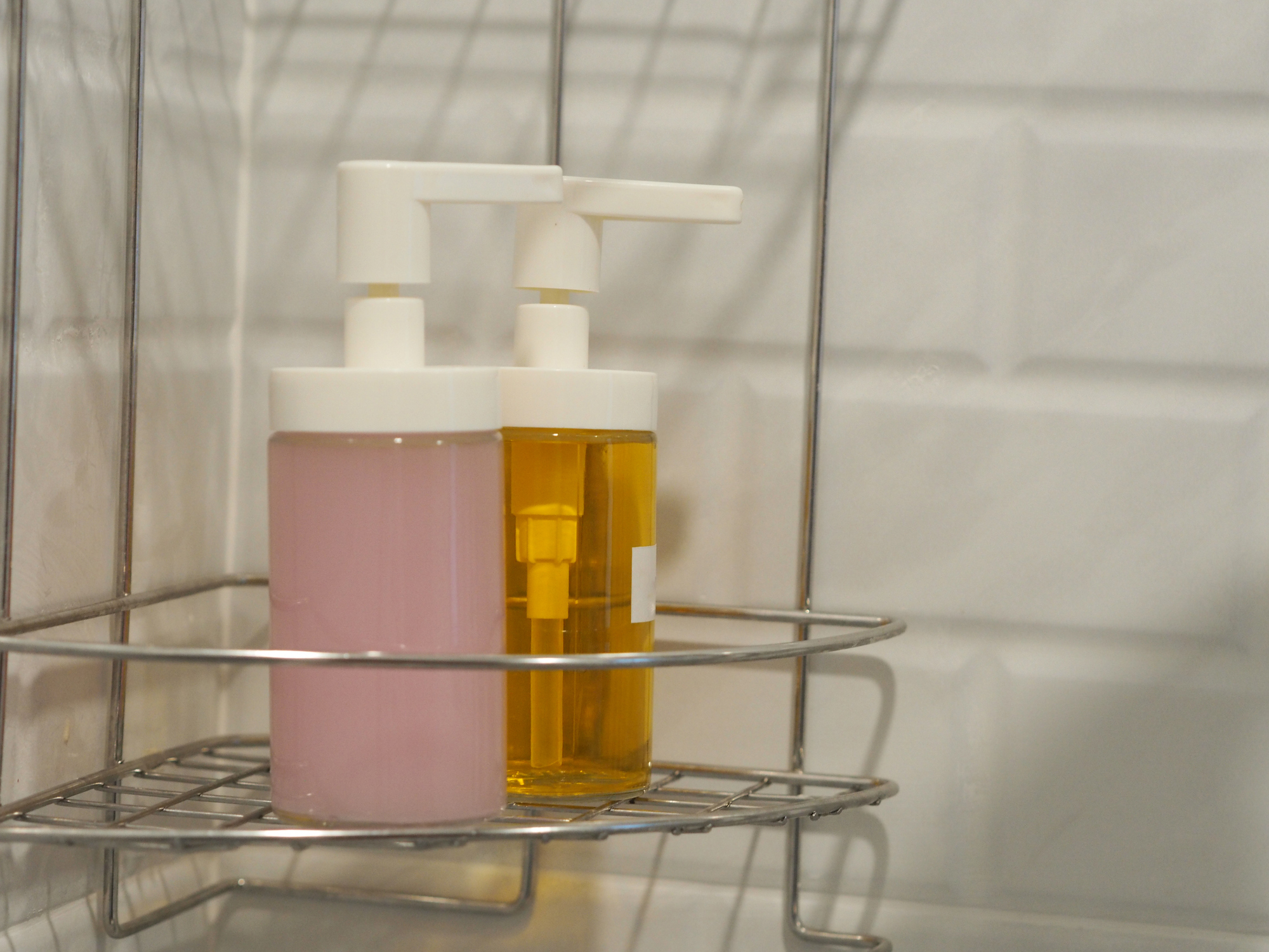 Two pump bottles, one with pink liquid and the other with yellow liquid, on a wire shelf in a shower