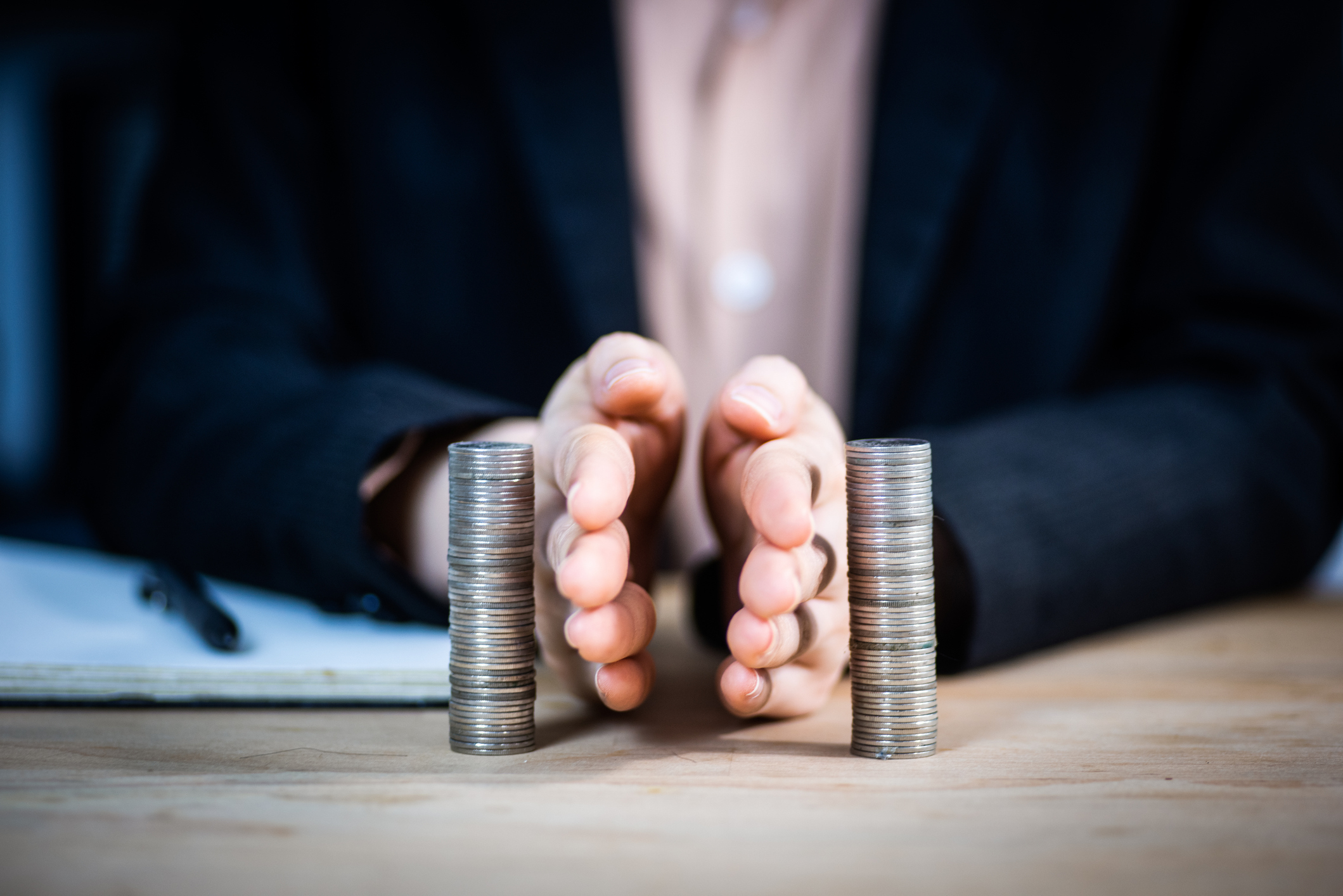A person wearing a suit uses their hands to separate two tall stacks of coins on a desk