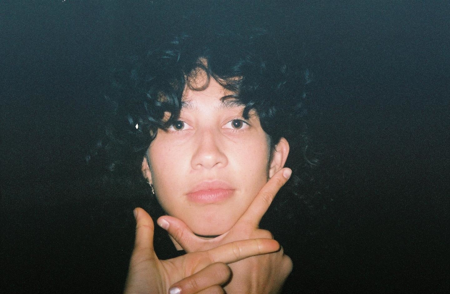 Person with curly hair making a hand gesture with crossed fingers in front of their face