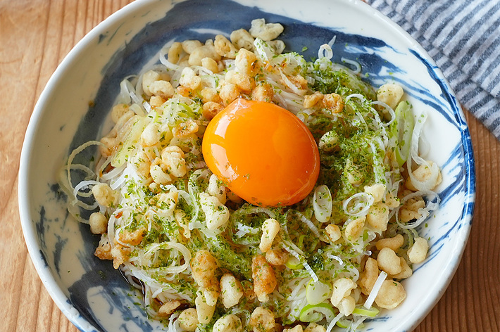 卵黄が中央にのった蕎麦の一皿。揚げ玉と刻みネギがトッピングされている。