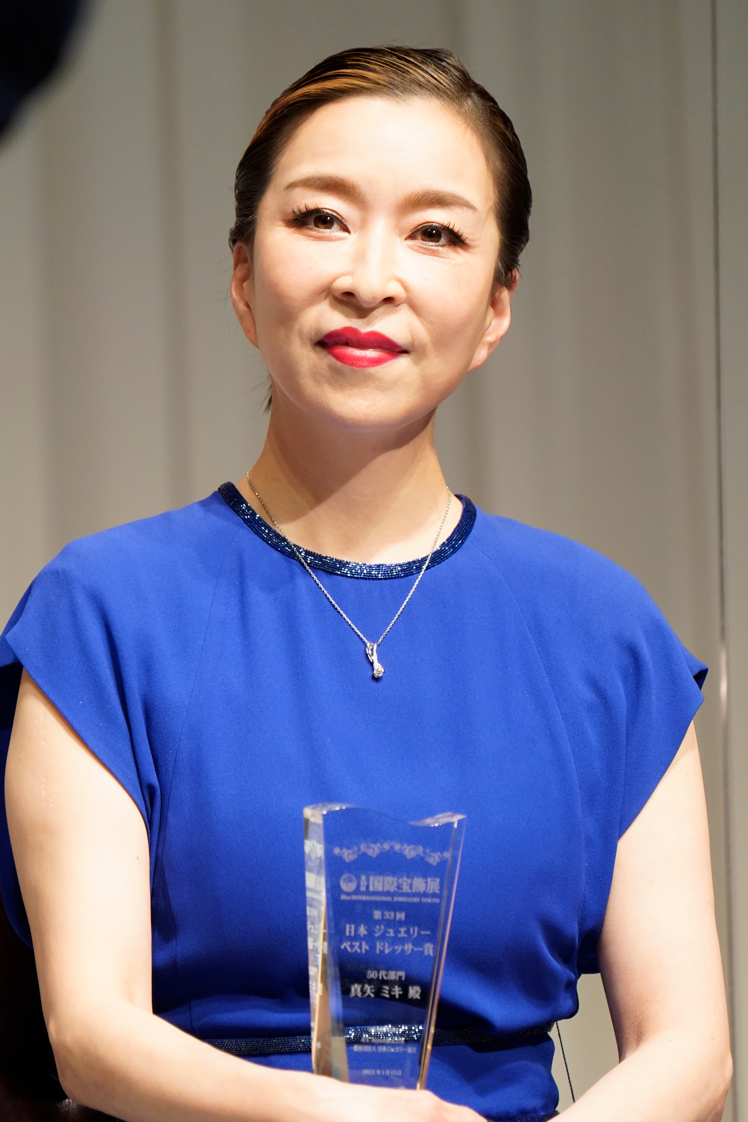 真矢ミキさんが青いドレスを着て、トロフィーを持ちながら舞台に立っています。