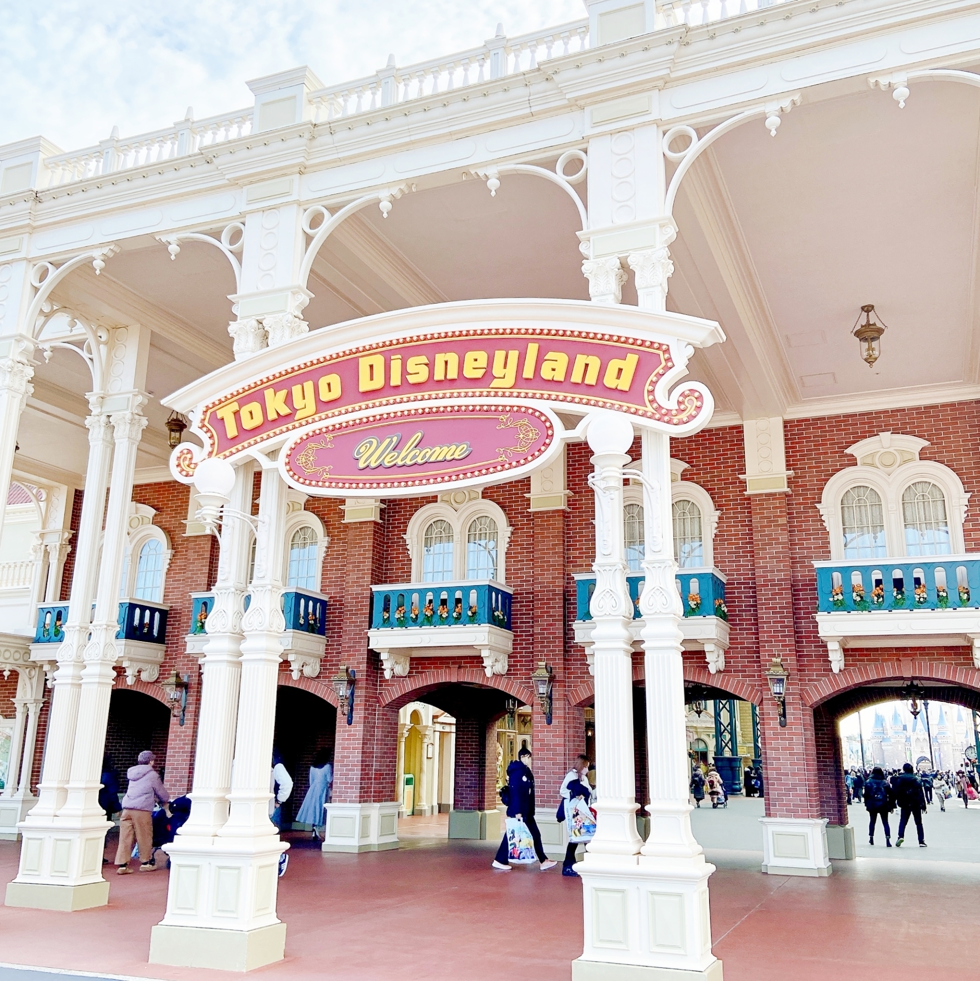 東京ディズニーランドの入口にあるウェルカムサインと建物。何人かの人々が歩いている。