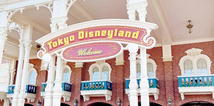 東京ディズニーランドの入口にあるウェルカムサインと建物。何人かの人々が歩いている。