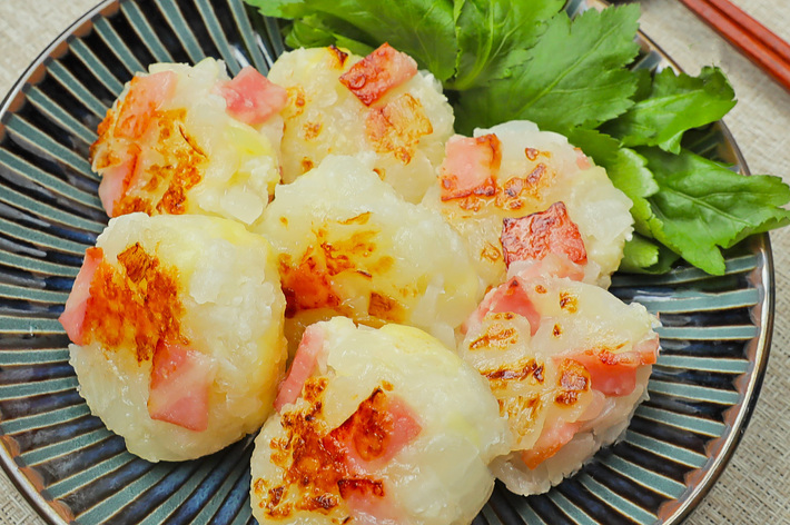 皿に盛られた焼きおにぎりに似た料理。上にはハムや葉野菜が添えられている。