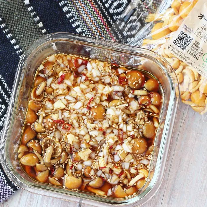 四角いガラス容器に入った玉ねぎ、ニンニク、ゴマ、唐辛子のソースに漬けられたシイタケの料理。