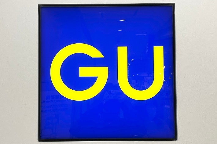 A square sign with the large yellow letters &ldquo;GU&rdquo; on a blue background