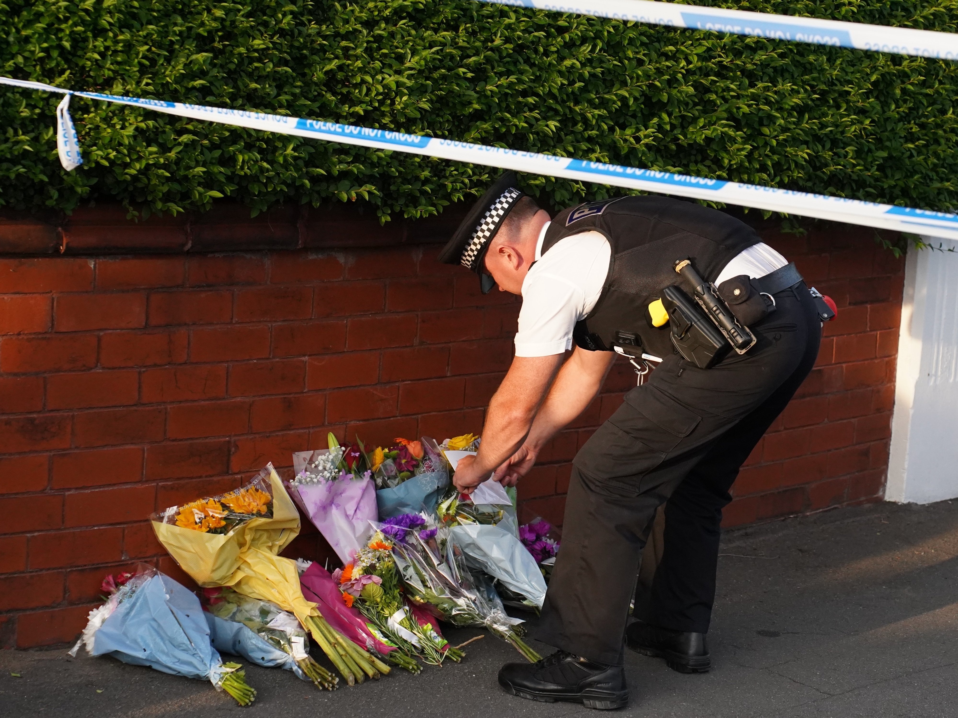 A police officer places floral tributes at a memorial site marked by police tape, dedicated to an unknown person