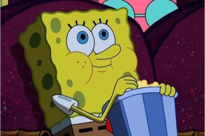 SpongeBob SquarePants sits on a couch, holding a bucket of popcorn, looking excited