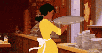 Tiana from "The Princess and the Frog" balances a tray while working in a kitchen.