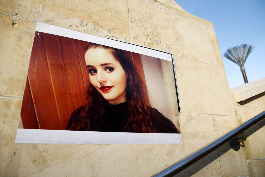 Large printout of a woman's portrait with long hair and red lipstick, posted on a stone wall next to a staircase