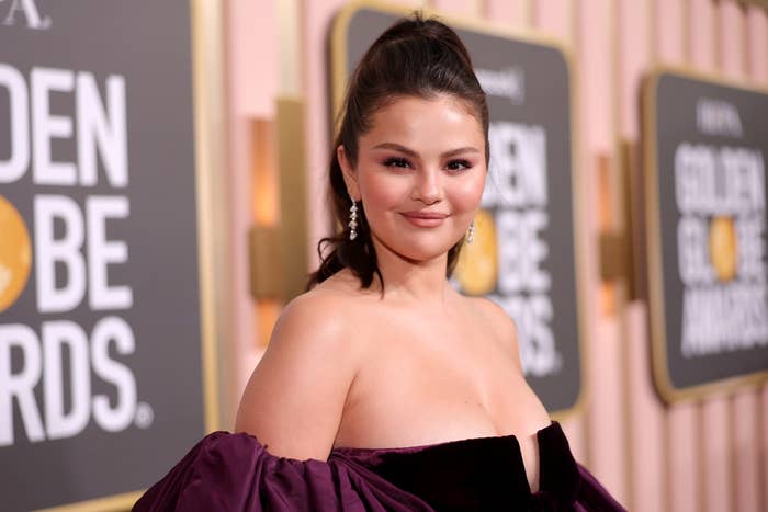 Selena Gomez on the red carpet at the Golden Globe Awards, wearing an elegant off-the-shoulder dress with drop earrings and a high ponytail