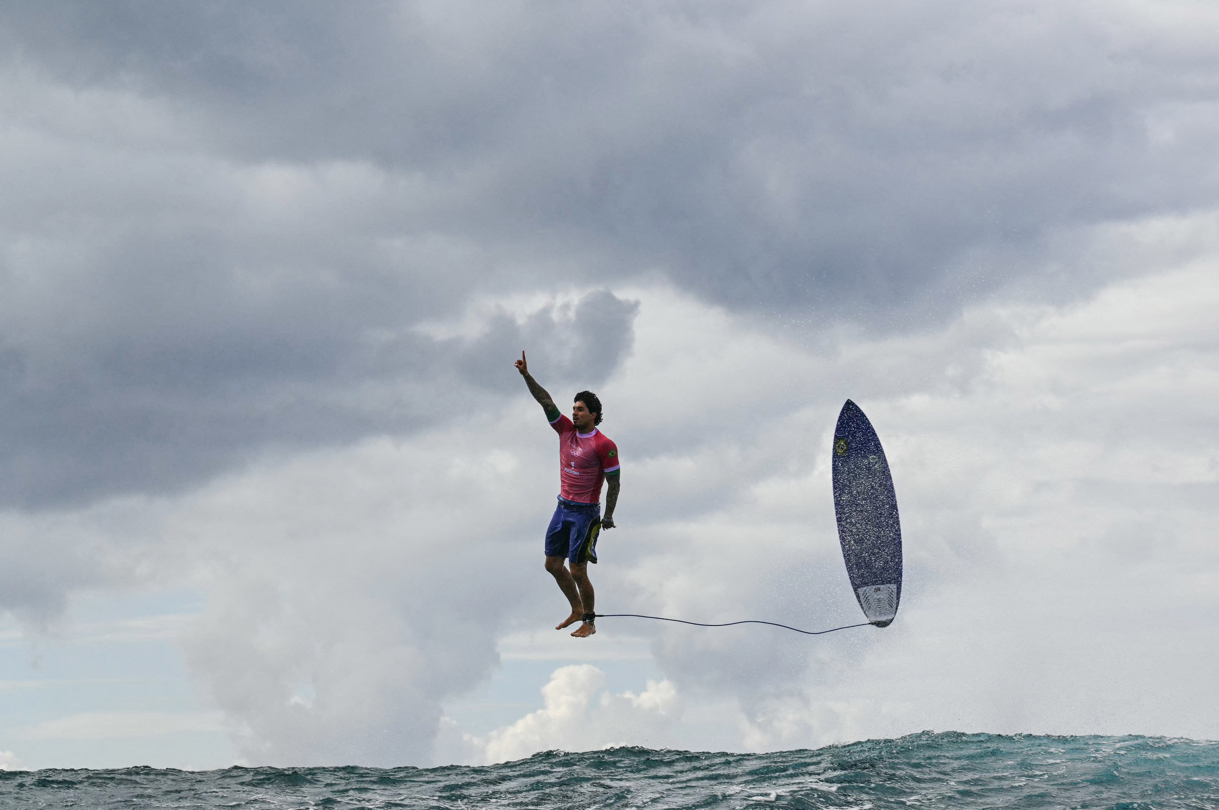 Man appearing to levitate above the ocean while holding his surfboard, under a cloudy sky