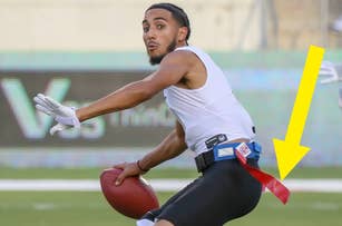 A man playing flag football is running with the ball. He has one flag on his belt, looking behind him with a focused expression