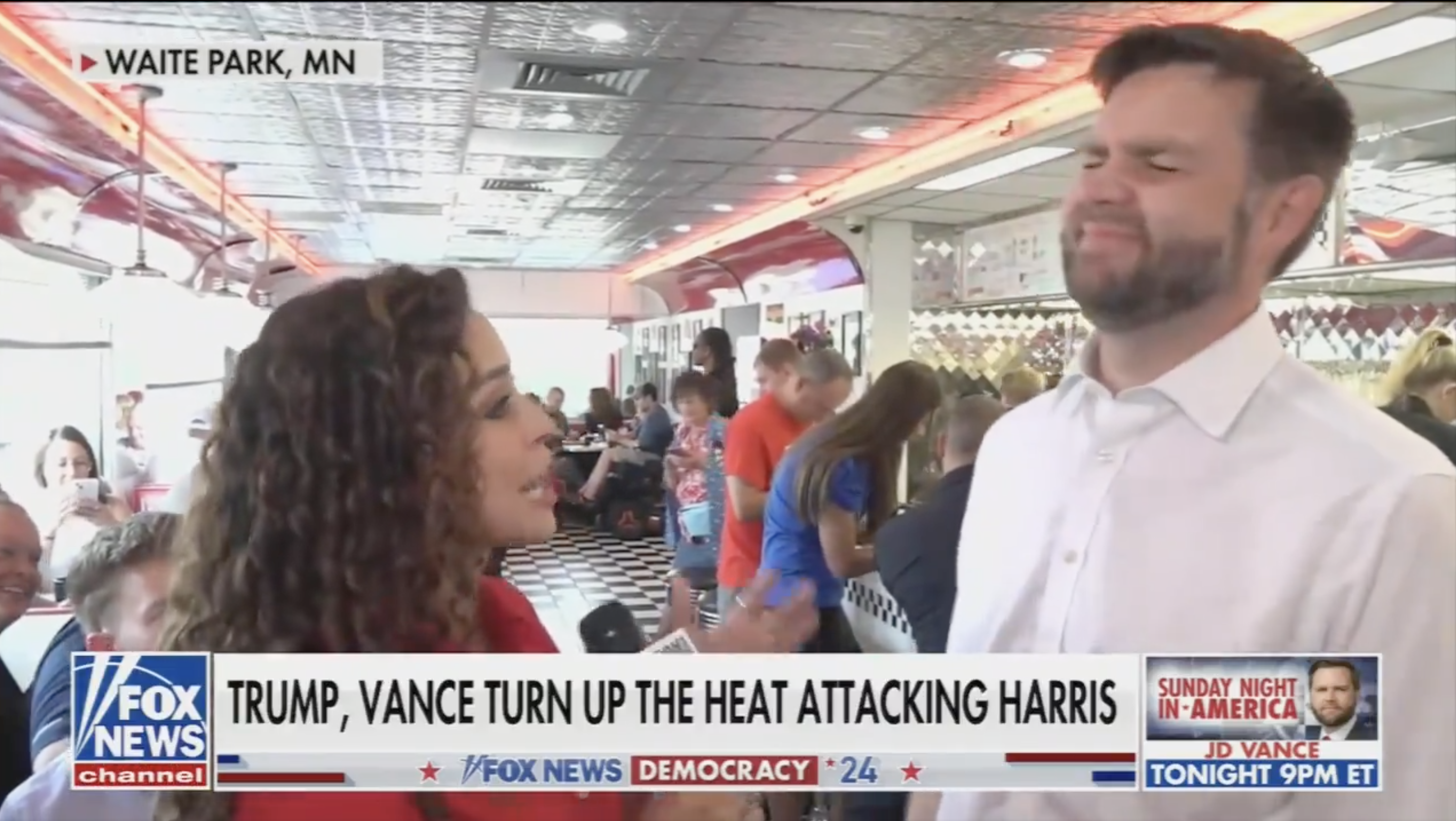 Video still from Fox News of reporter interviewing J.D. Vance in a diner in Waite Park, MN. Overlay text mentions Trump and Vance attacking Harris