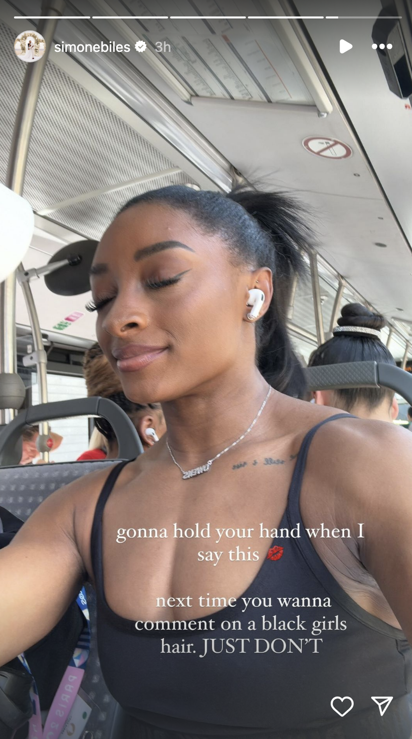 Simone Biles is on a bus, wearing earbuds and a sleeveless top. Text over the image reads: "gonna hold your hand when I say this. next time you wanna comment on a black girl's hair. JUST DON’T."