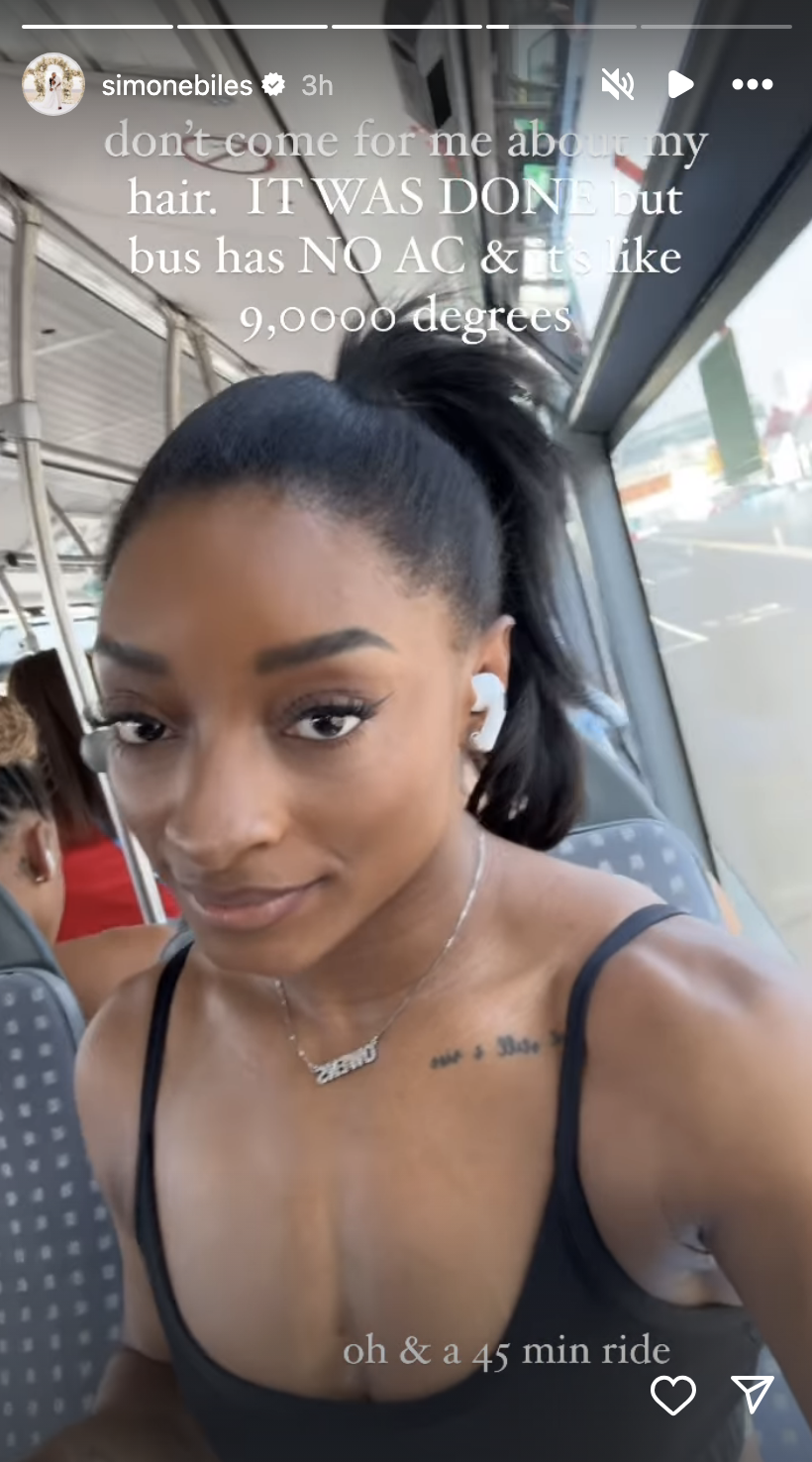 Simone Biles on a bus, hair in a ponytail, wearing a necklace and earphones. Caption mentions her hair, no AC, and a 45-minute ride