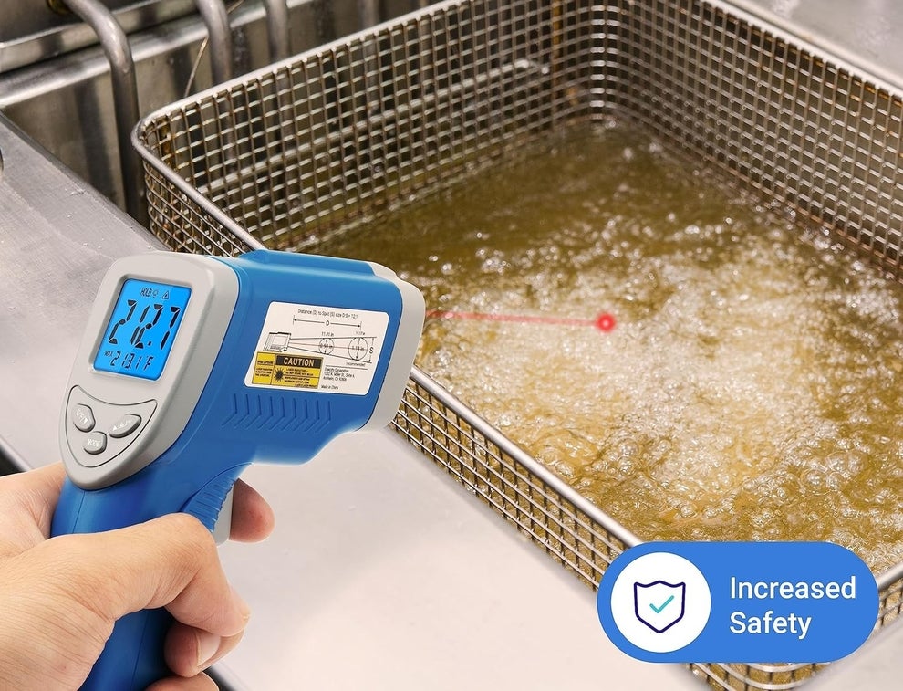 Hand using a digital non-contact thermometer to measure oil temperature in an industrial fryer. Text promotes safe measurements and increased safety