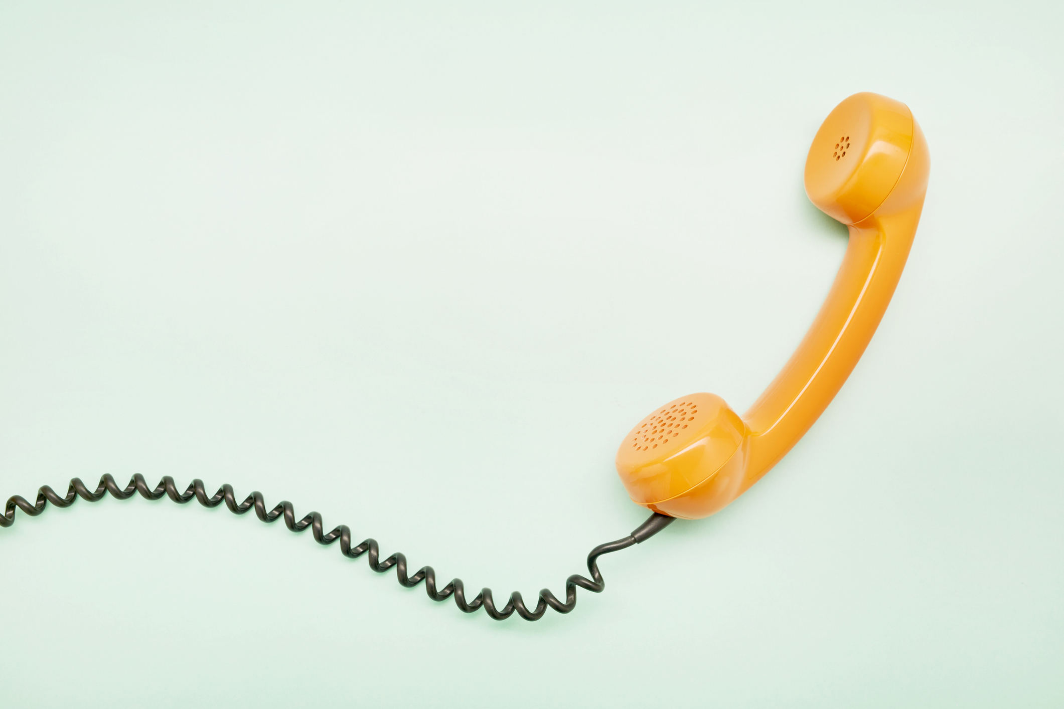 An orange vintage corded telephone handset, placed on a light background with its curly cord extending from the left side