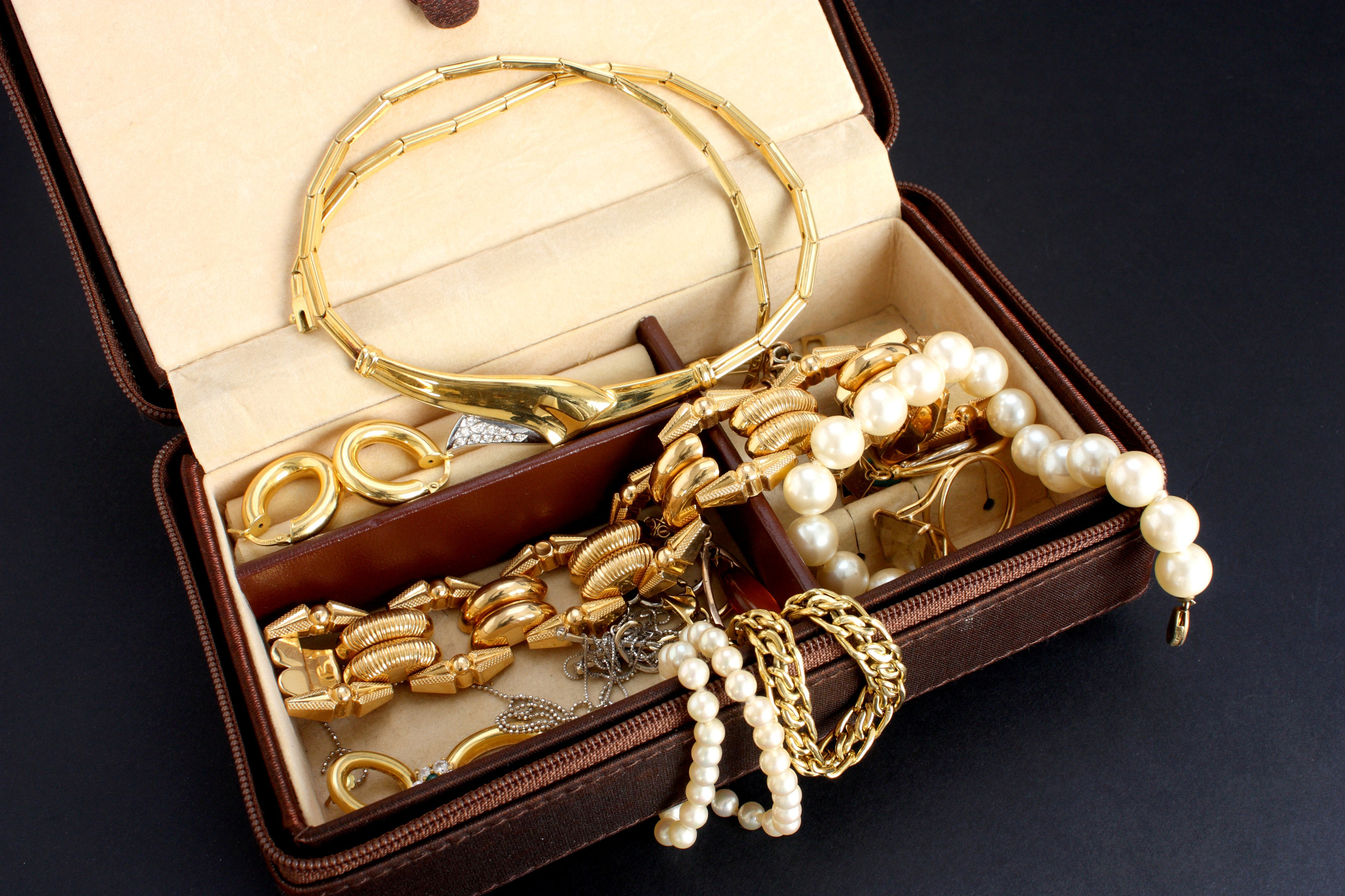 An open jewelry box showing a collection of gold accessories and pearl necklaces