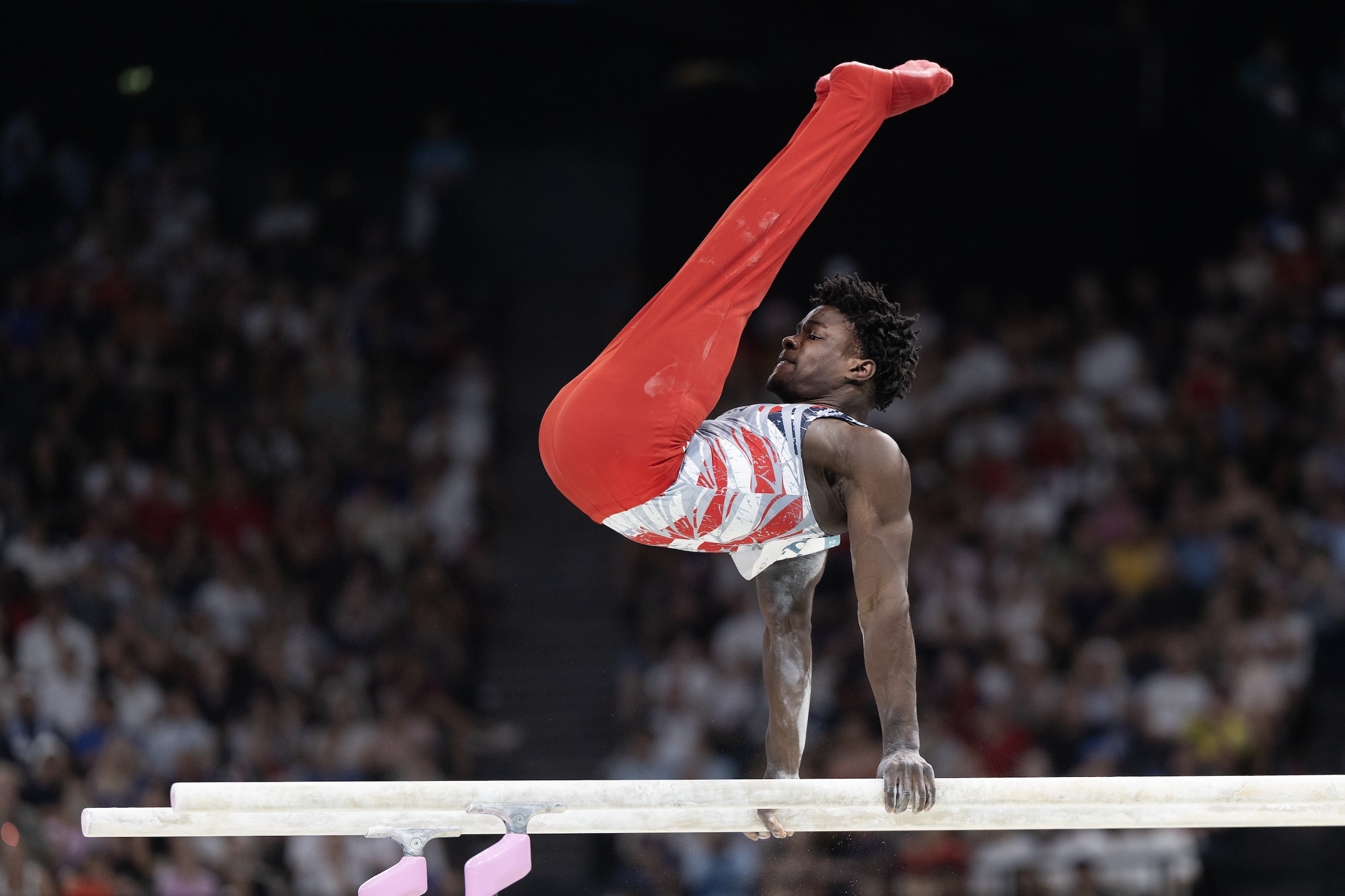 Gymnast performs on pommel horse in a dynamic pose, audience in background